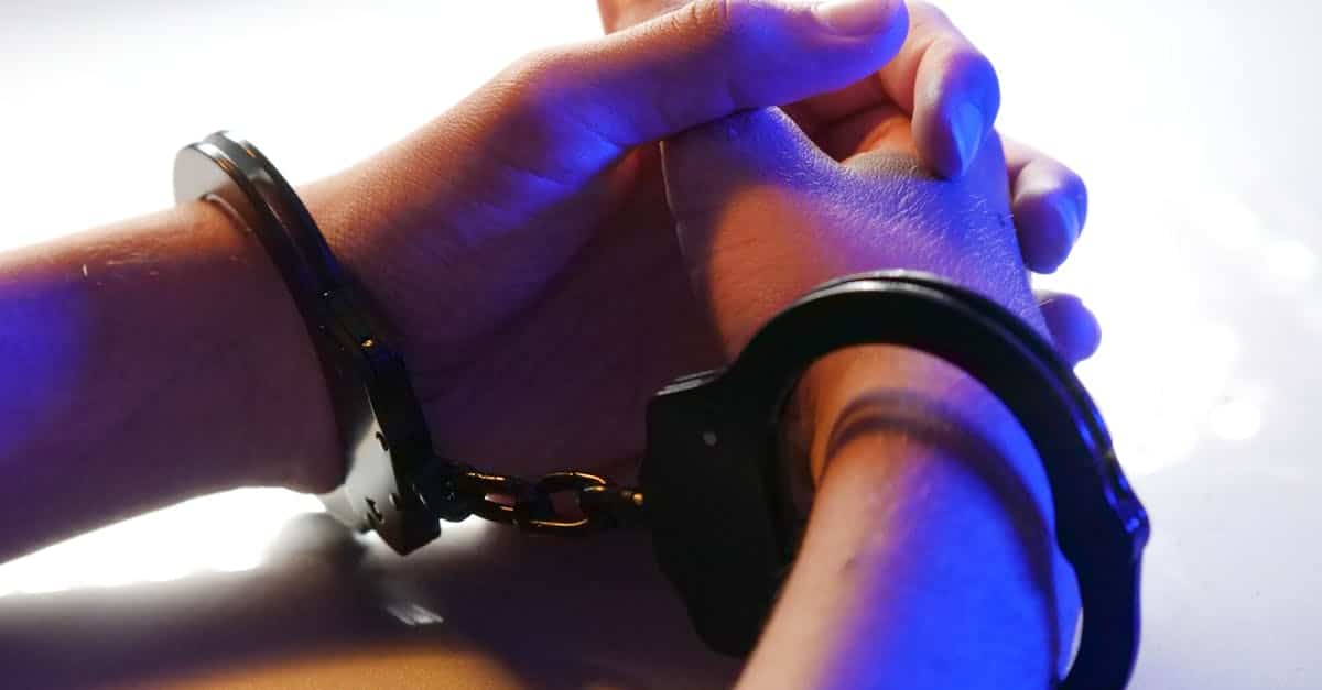 Close-up of handcuffed hands under blue police light, signifying arrest or detention.